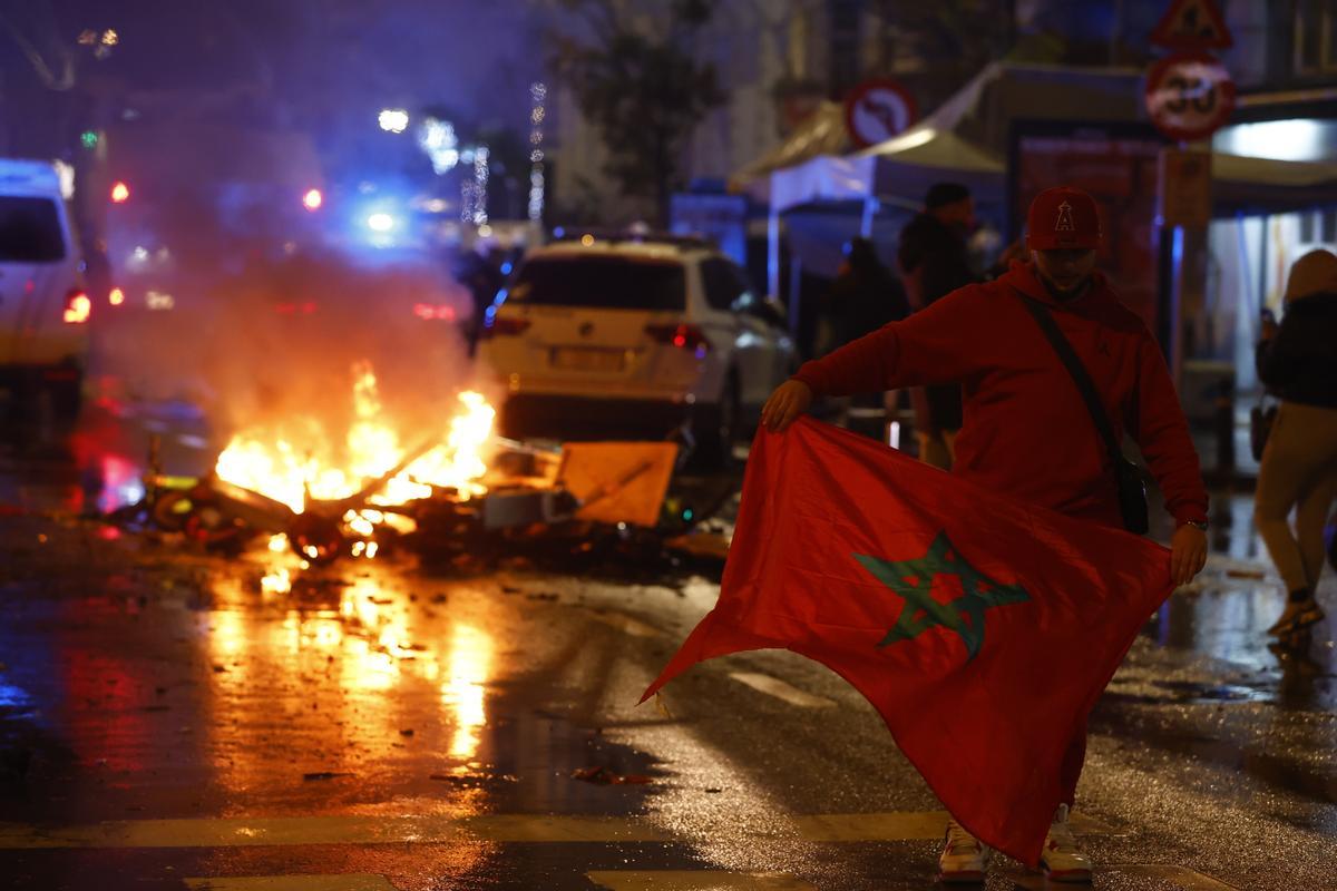 Un aficionado con la bandera de Marruecos en una calle de Bruselas con un foco de incendio al fondo.
