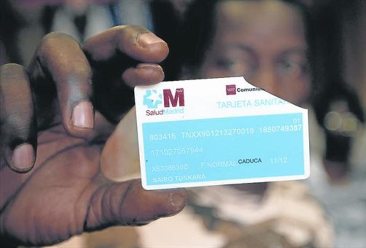 Una inmigrante muestra una tarjeta sanitaria rota de la Comunidad de Madrid, por la retirada del derecho.