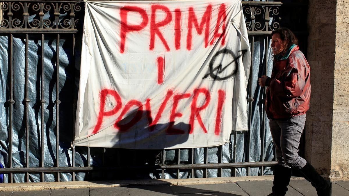 Angela Grossi, desalojada de una vivienda abandonada, pasa junto a una pintada en una sábana que reza ’Primero los pobres’, colgada en el pórtico de la basílica de los Santos Apóstoles, en Roma, el 29 de enero. Angela Grossi, desalojada de una vivienda abandonada, pasa junto a una pintada en una sábana que reza ’Primero los pobres’, colgada en el pórtico de la basílica de los Santos Apóstoles, en Roma, el 29 de enero.