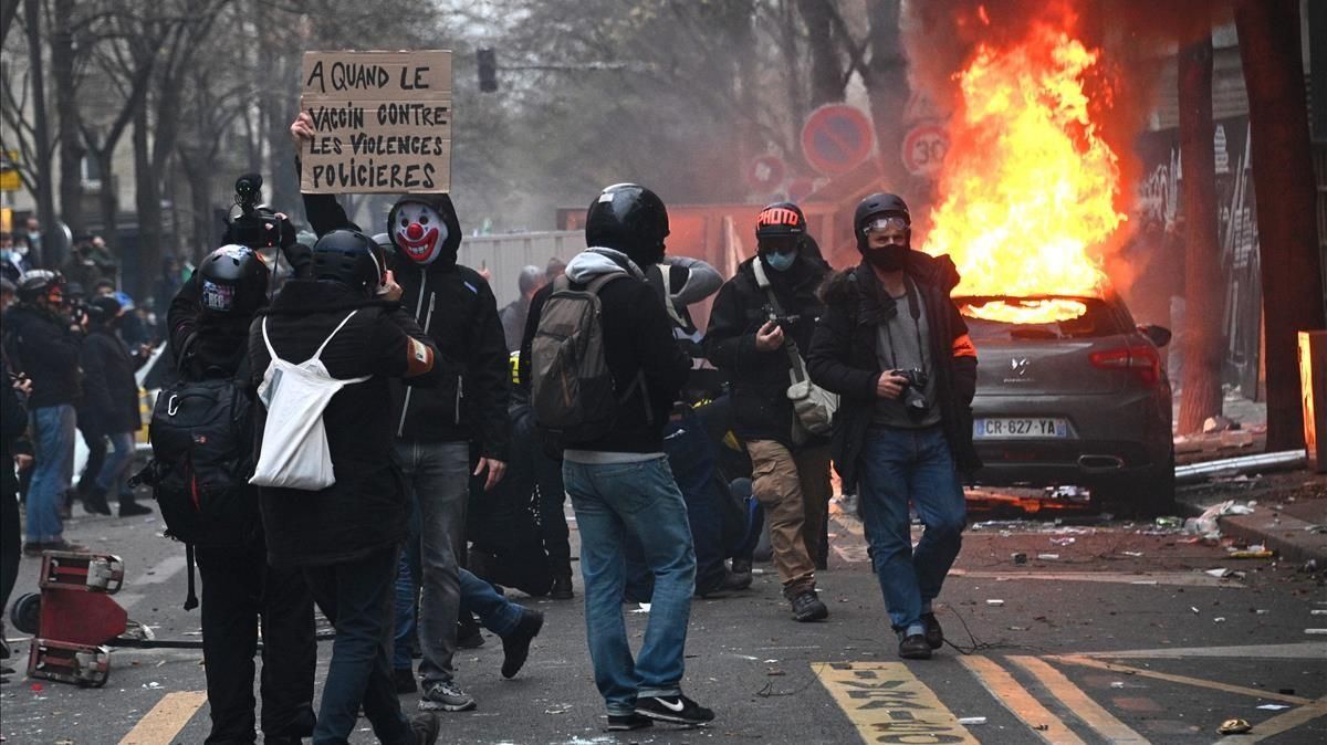 Un manifestantes muestra un cartel contra la violencia policial en una calle donde se ha prendido fuego a un vehículo aparcado. Un manifestantes muestra un cartel contra la violencia policial en una calle donde se ha prendido fuego a un vehículo aparcado.