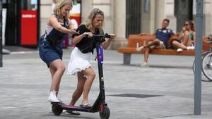 Dos jóvenes intentan subirse a un patinete compartido en Barcelona, en agosto de 2019, cuando las empresas operaban sin paraguas legal.