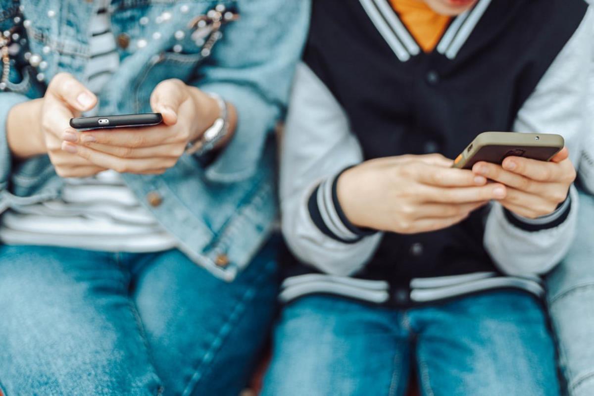 Dos adolescentes atentos a las pantallas de sus teléfonos móviles.
