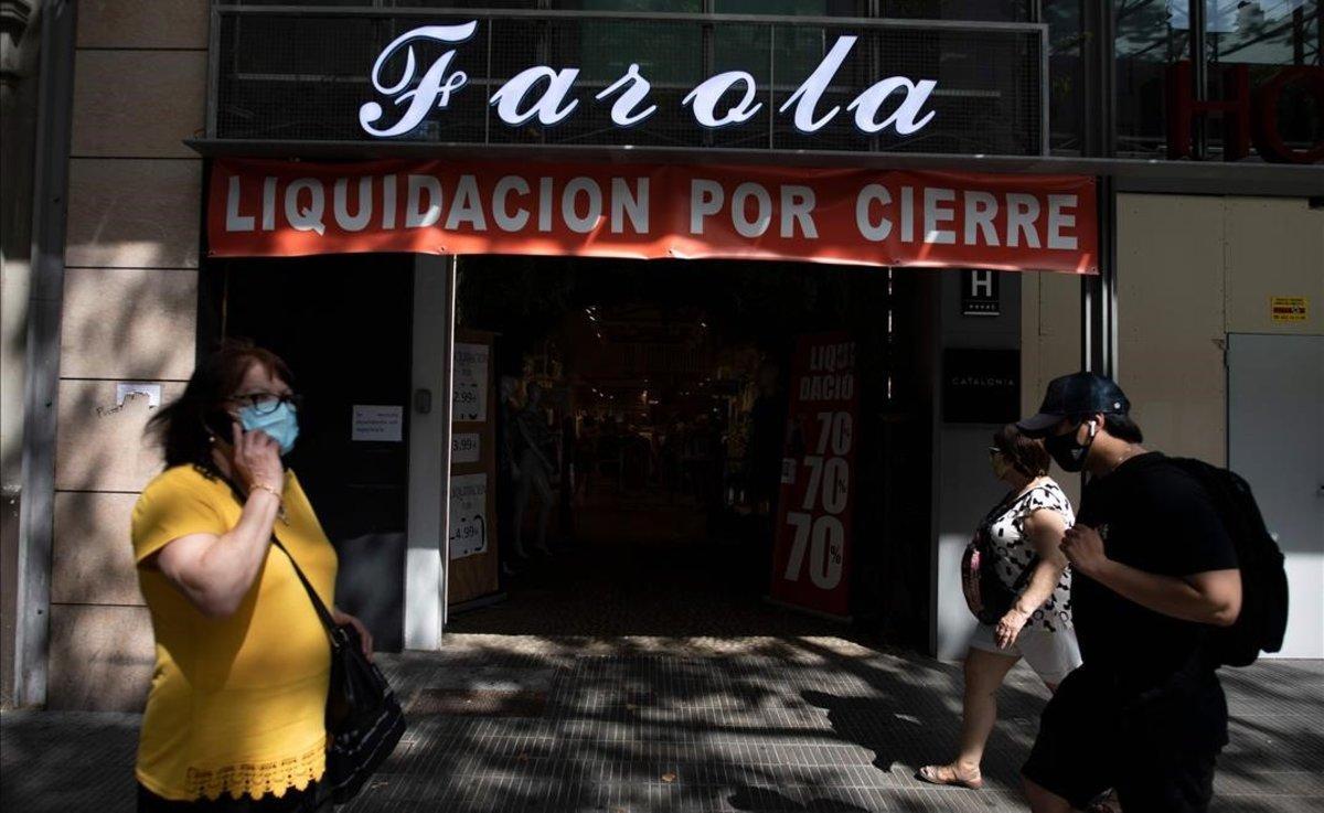 Ciudadanos pasan frente a una tienda cerrada tras la crisis del coronavirus, en el centro de Barcelona.