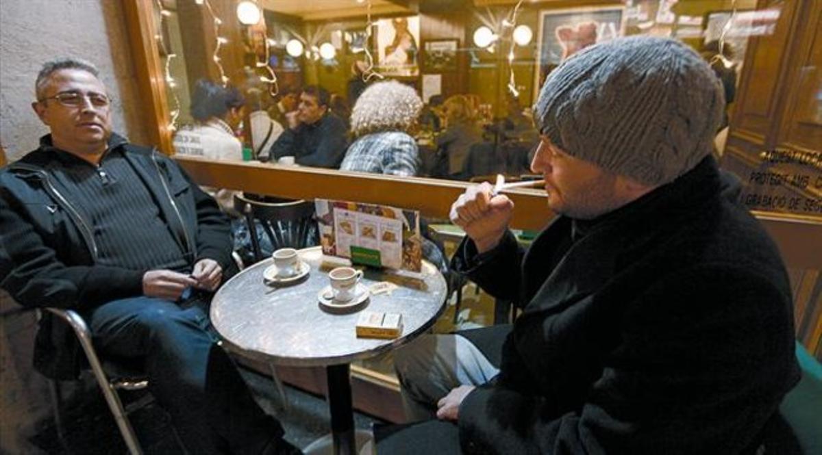Un hombre enciende un cigarrillo en la terraza exterior de una cafetería de la calle de Casp de Barcelona, ayer por la tarde, primer día de la prohibición total de tabaco en locales cerrados.