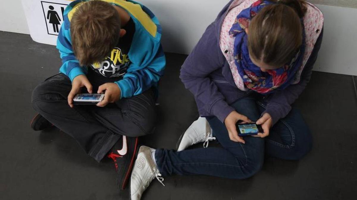 Dos niños atentos a la pantalla de su móvil.