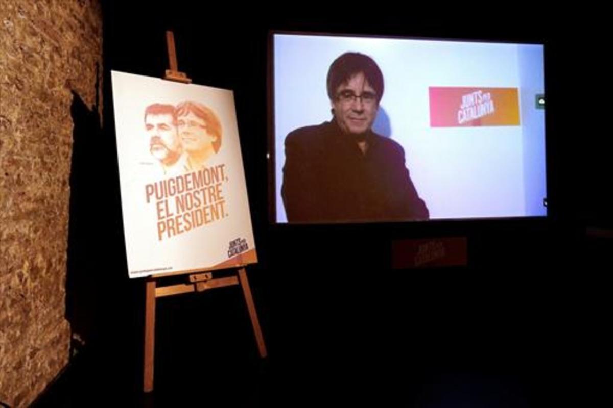 Videoconferencia de Puigdemont, junto a un cartel de Junts per Catalunya.