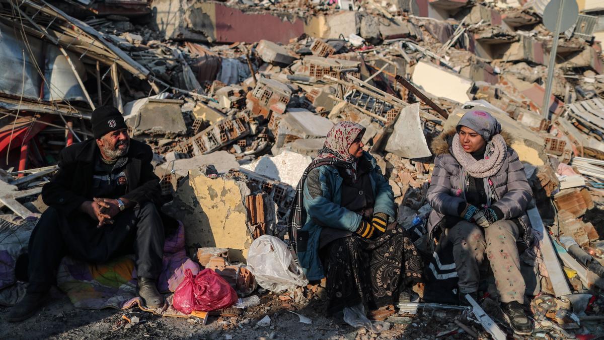 Personas sentadas junto a un edificio derrumbado tras el terremoto en Hatay, Turquía  