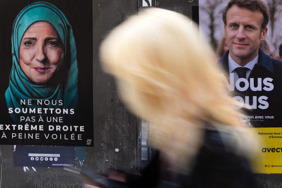 Una mujer pasa ante un carte electoral de Macron y Le Pen, ella con velo musulmán.