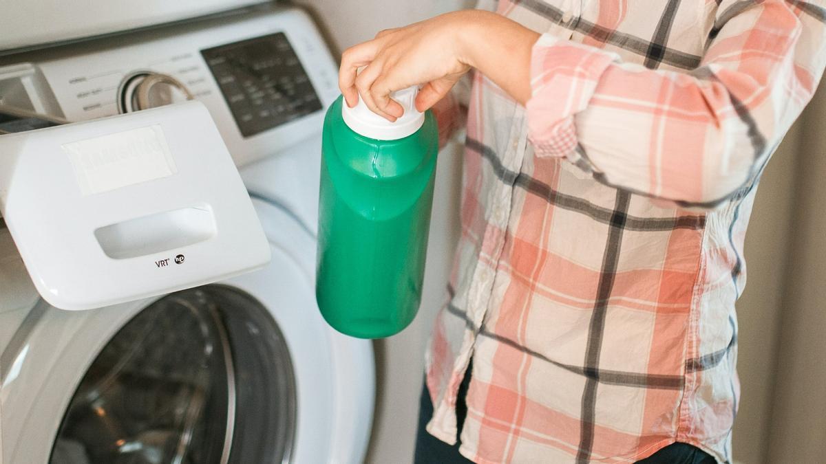 Una persona destapa el detergente para poner la lavadora.
