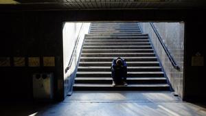 Un joven sentado en las escaleras de la boca del metro