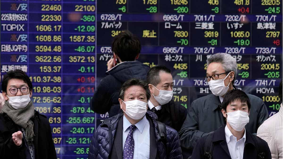 El coronavirus podría costar más de 300.000 millones a la economía mundial. En la foto, ciudadanos protegidos con mascarillas pasan frente a pantallas con información bursatil en Tokio.