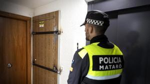 Un policía municipal de Mataró, junto a una puerta que los vecinos han blindado con barras para evitar que la vivienda sea ocupada.