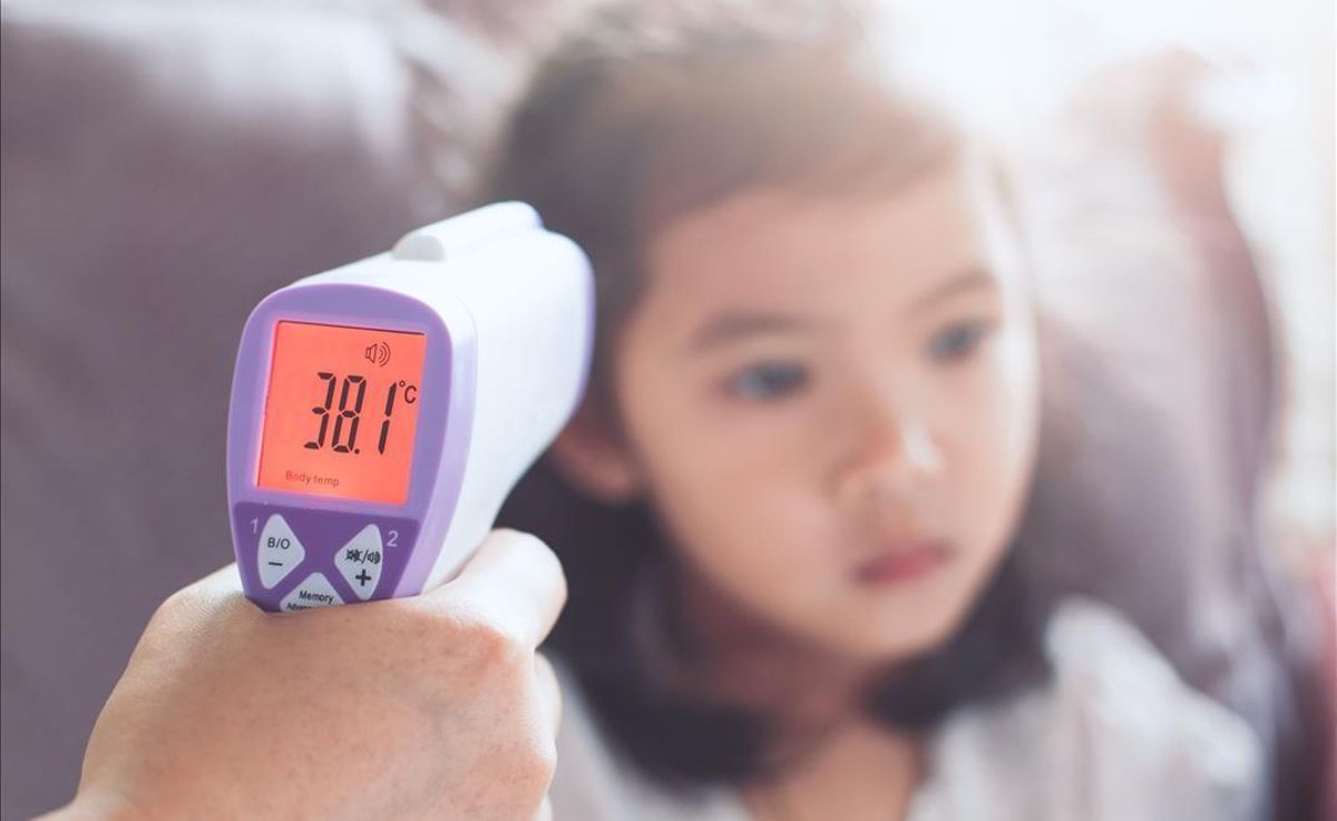 Una madre toma la temperatura a su hija con un termómetro de infrarrojos. Una madre toma la temperatura a su hija con un termómetro de infrarrojos.