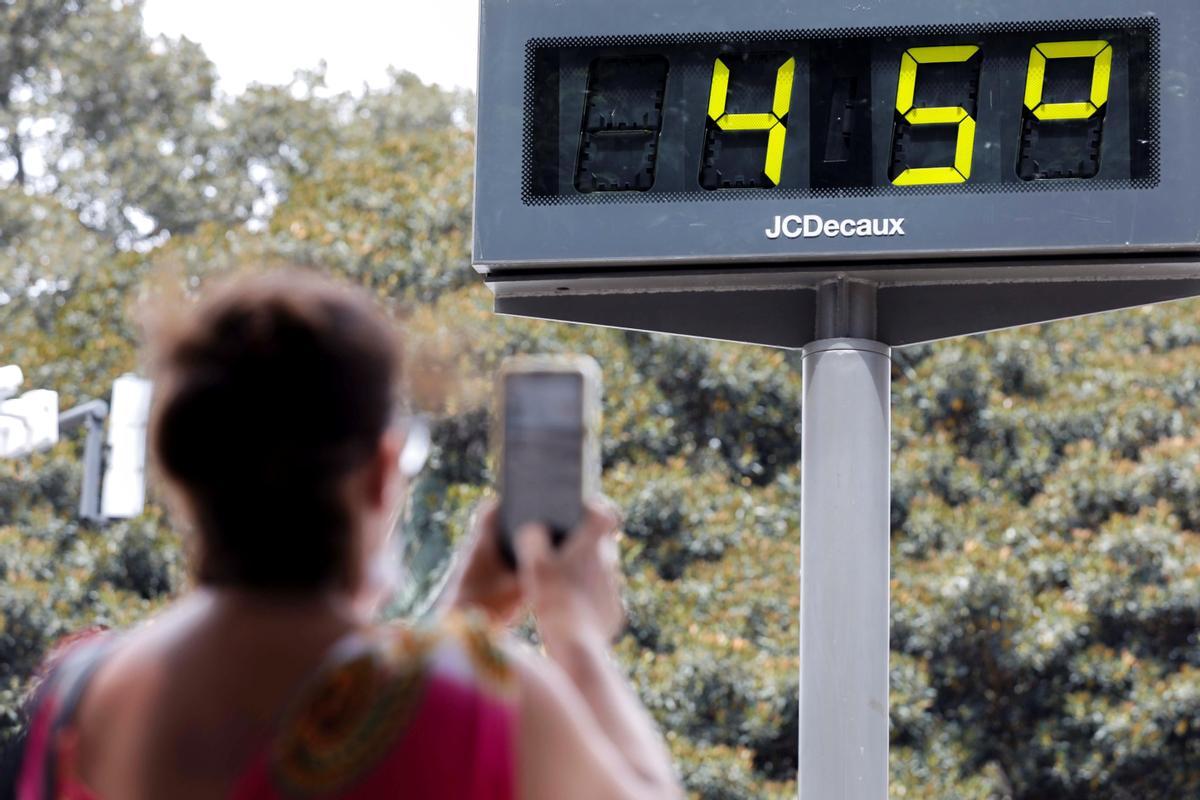 Una mujer toma una fotografía de un termómetro urbano marcando 45º.