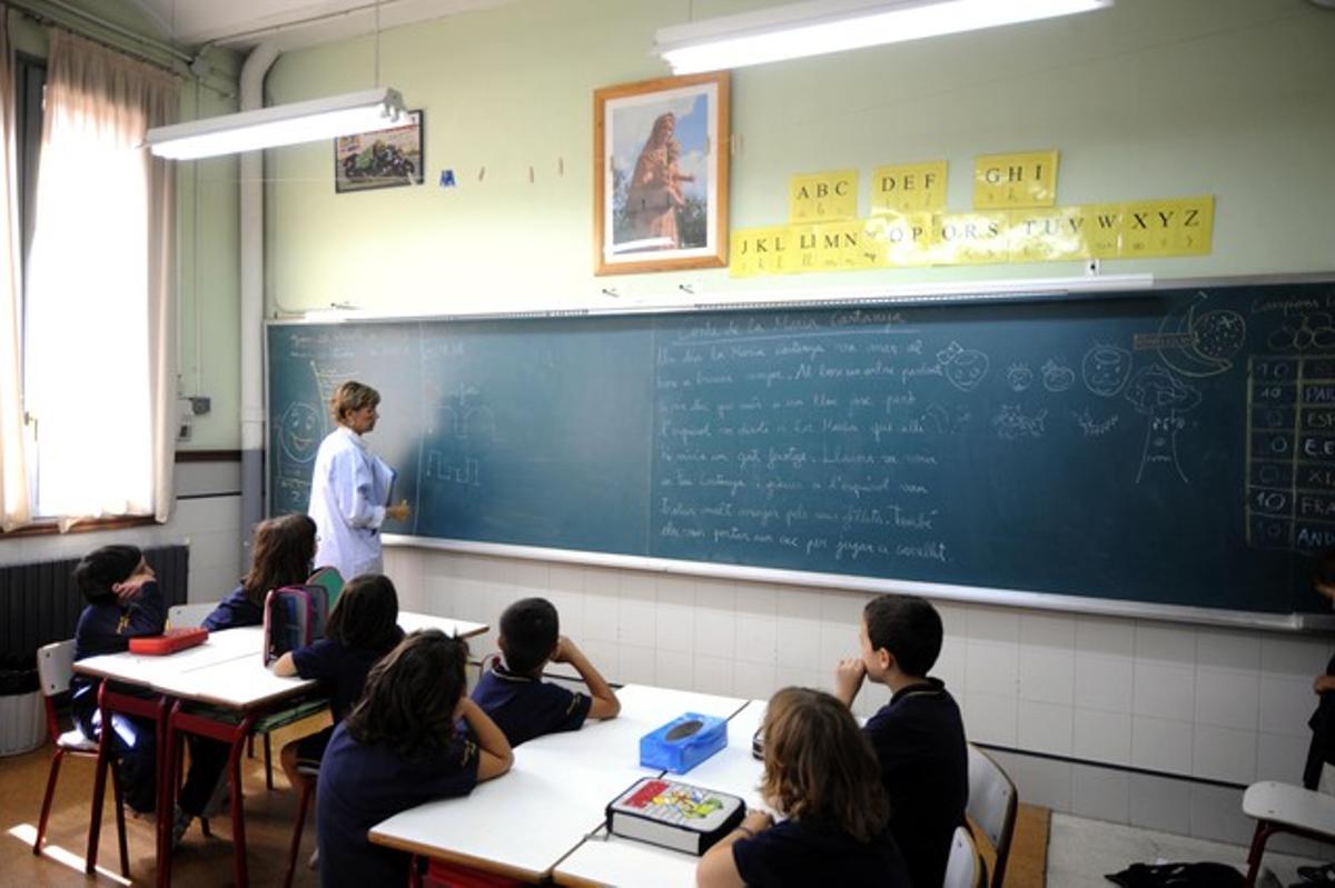 Una profesora da clases a niños de segundo de Primaria en un colegio de Lleida con una imagen de una Virgen en la pared frontal.