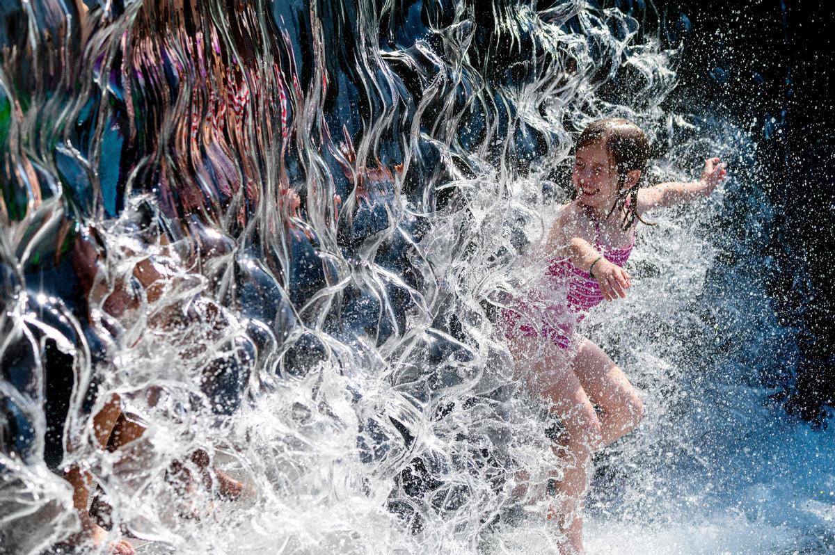 Una niña se refresca en una cascada de agua en un parque en Washington DC.