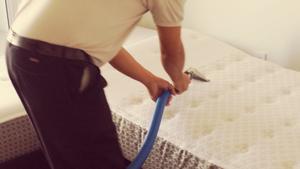 Un hombre limpia un colchón con un aspirador.