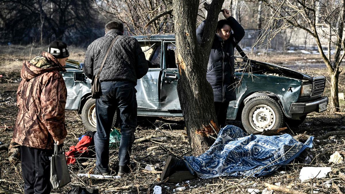 People stand by the body of a relative stretched out on the ground after bombings on the eastern Ukraine town of Chuguiv on February 24, 2022, as Russian armed forces are trying to invade Ukraine from several directions, using rocket systems and helicopters to attack Ukrainian position in the south, the border guard service said. - Russias ground forces on Thursday crossed into Ukraine from several directions, Ukraines border guard service said, hours after President Vladimir Putin announced the launch of a major offensive. Russian tanks and other heavy equipment crossed the frontier in several northern regions, as well as from the Kremlin-annexed peninsula of Crimea in the south, the agency said. (Photo by Aris Messinis / AFP)