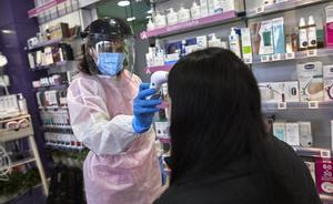 Una farmacéutica toma la temperatura a una mujer antes de realizarle un test de antígenos en la Farmacia Las Gemelas en Madrid.