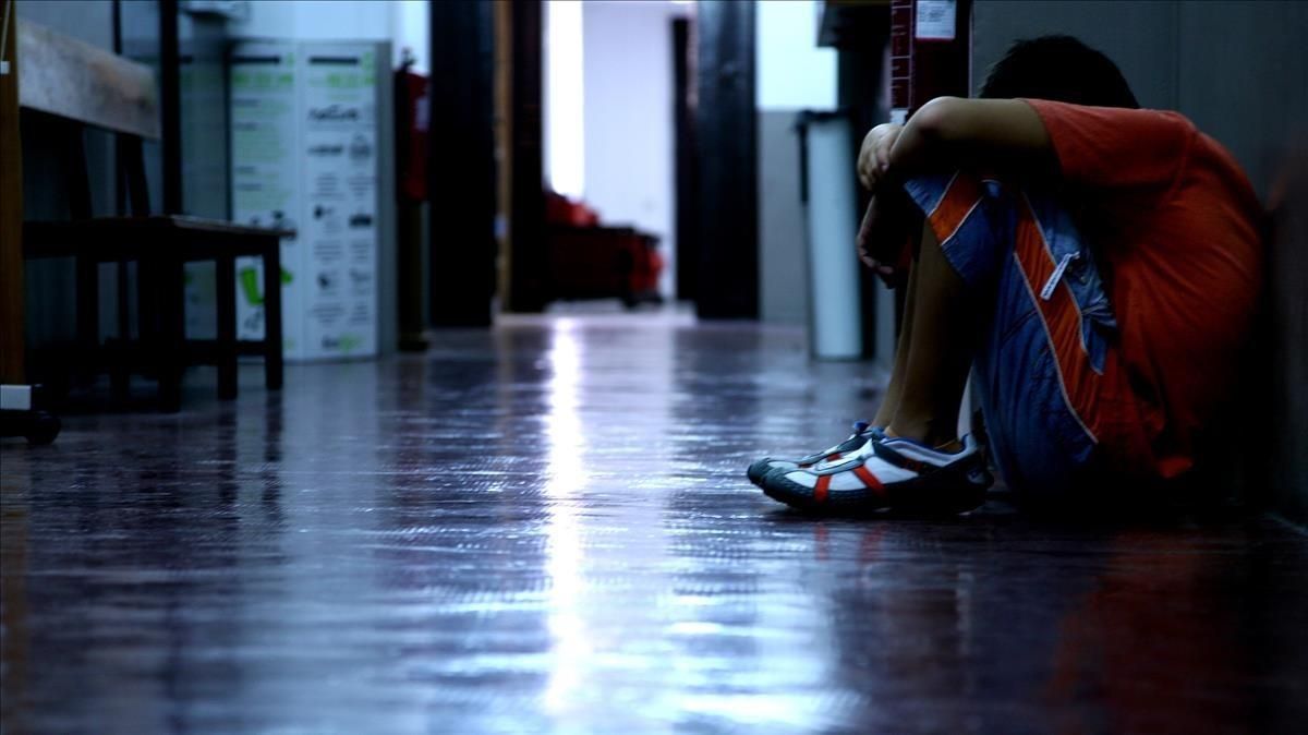 Un adolescente se oculta la cara sentado en el pasillo de su instituto. Un adolescente se oculta la cara sentado en el pasillo de su instituto.