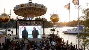 Personas miran en una pantalla gigante la presentación del retorno de Abba, en Estocolmo, mientras Bjoern Ulvaeus y Benny Andersson hablan en el evento.