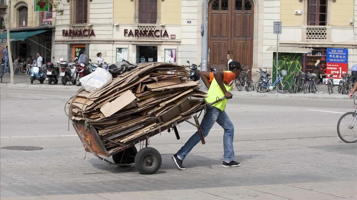 Un nmigrante africano lleva un carrito lleno de cartones. Un nmigrante africano lleva un carrito lleno de cartones.