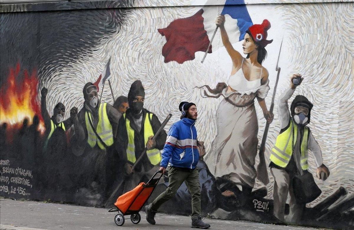 Un hombre pasa junto a un mural que reproduce una versión de ’La libertad guiando al pueblo’, de Eugene Delacroix, con la presencia de ’chalecos amarillos’, idea del artista Pascal Boyart. Un hombre pasa junto a un mural que reproduce una versión de ’La libertad guiando al pueblo’, de Eugene Delacroix, con la presencia de ’chalecos amarillos’, idea del artista Pascal Boyart.