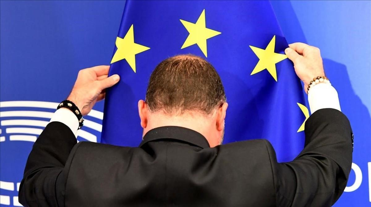 Un empleado del parlamento europeo coloca la bandera de la Unión Europea antes de la conferencia de prensa.