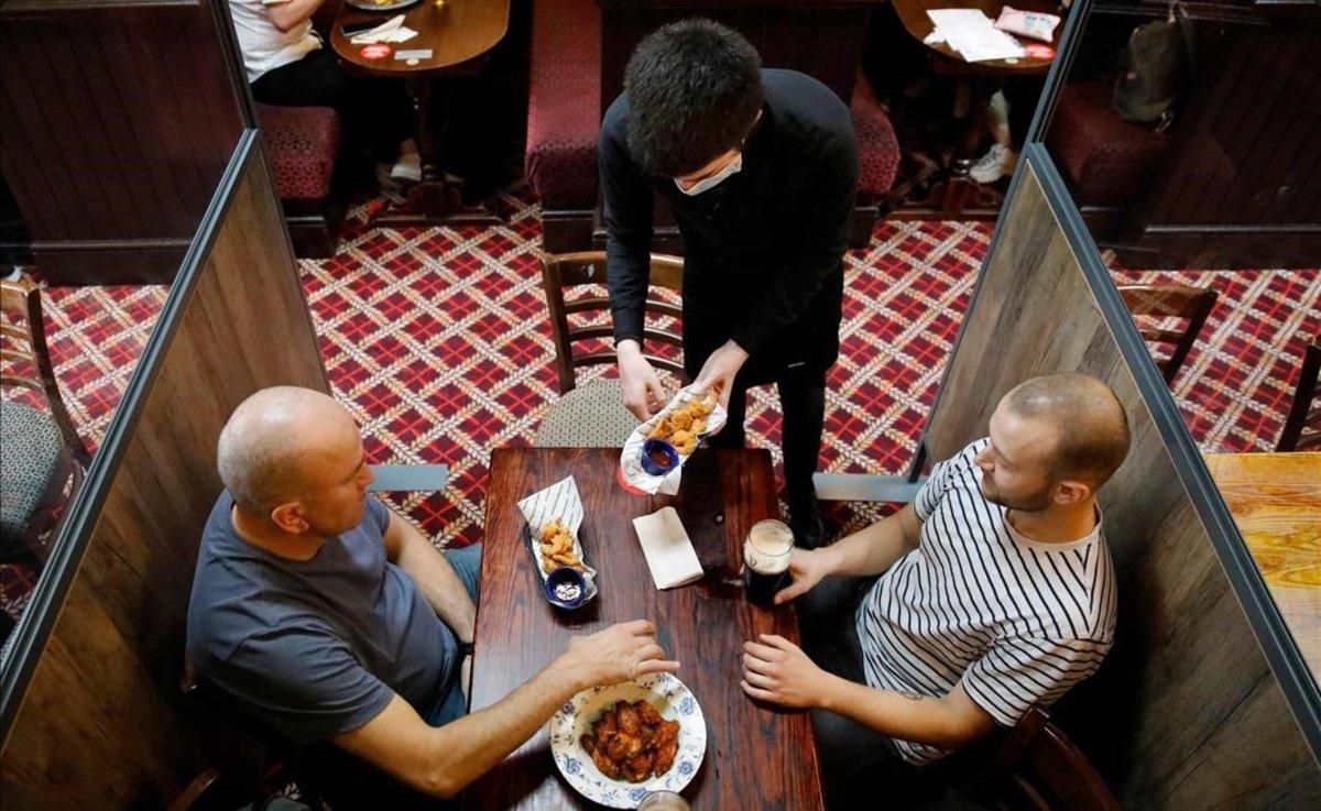 Un camarero protegido contra el covid sirve a los clientes en un pub de Londres. Un camarero protegido contra el covid sirve a los clientes en un pub de Londres.