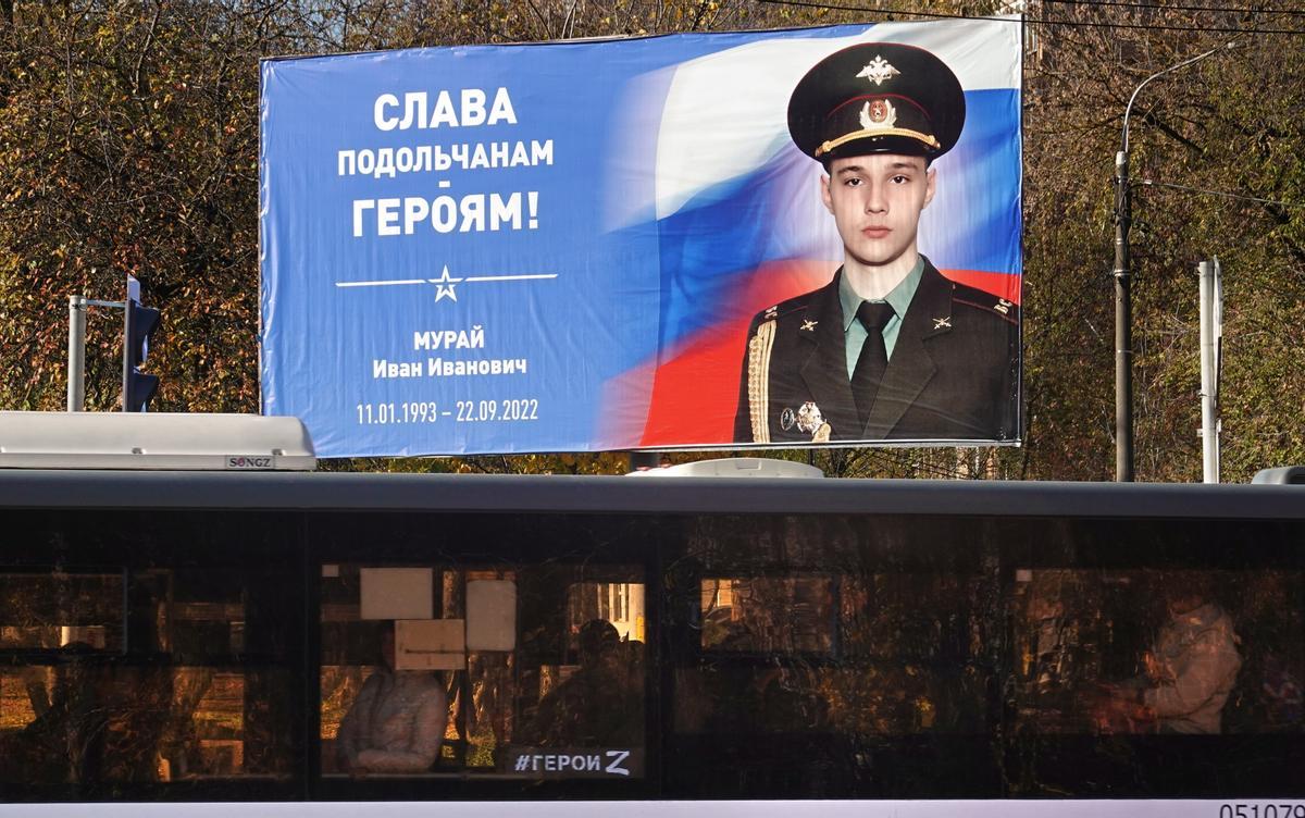 Un autobús con una pintada de la letra Z, en apoyo a la invasión de Ucrania, circula por un suburbio de Moscú junto a un poster con un retrato de un soldado ruso fallecido en la guerra.