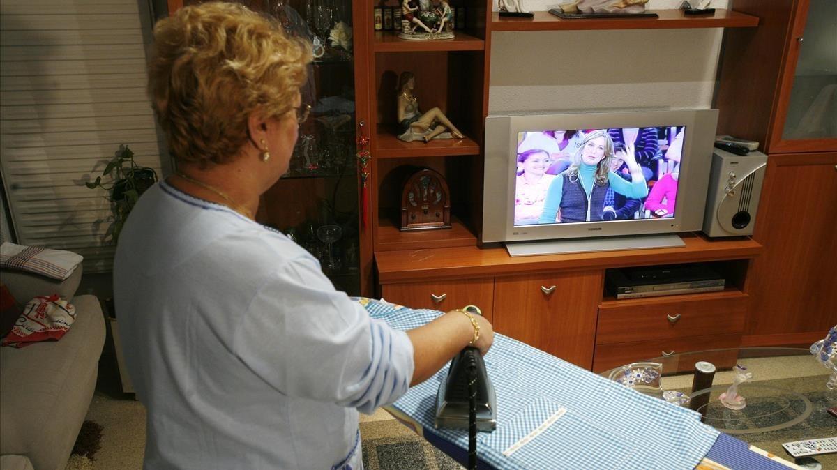 Ama de casa sigue un programa de televisión, mientras realiza labores del hogar.