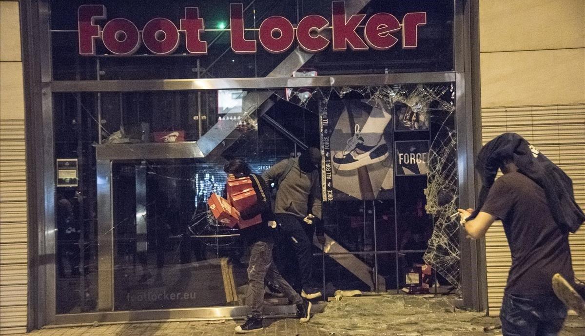 Un hombre sale con cajas de zapatos de la tienda Foot Locker, la noche del sábado