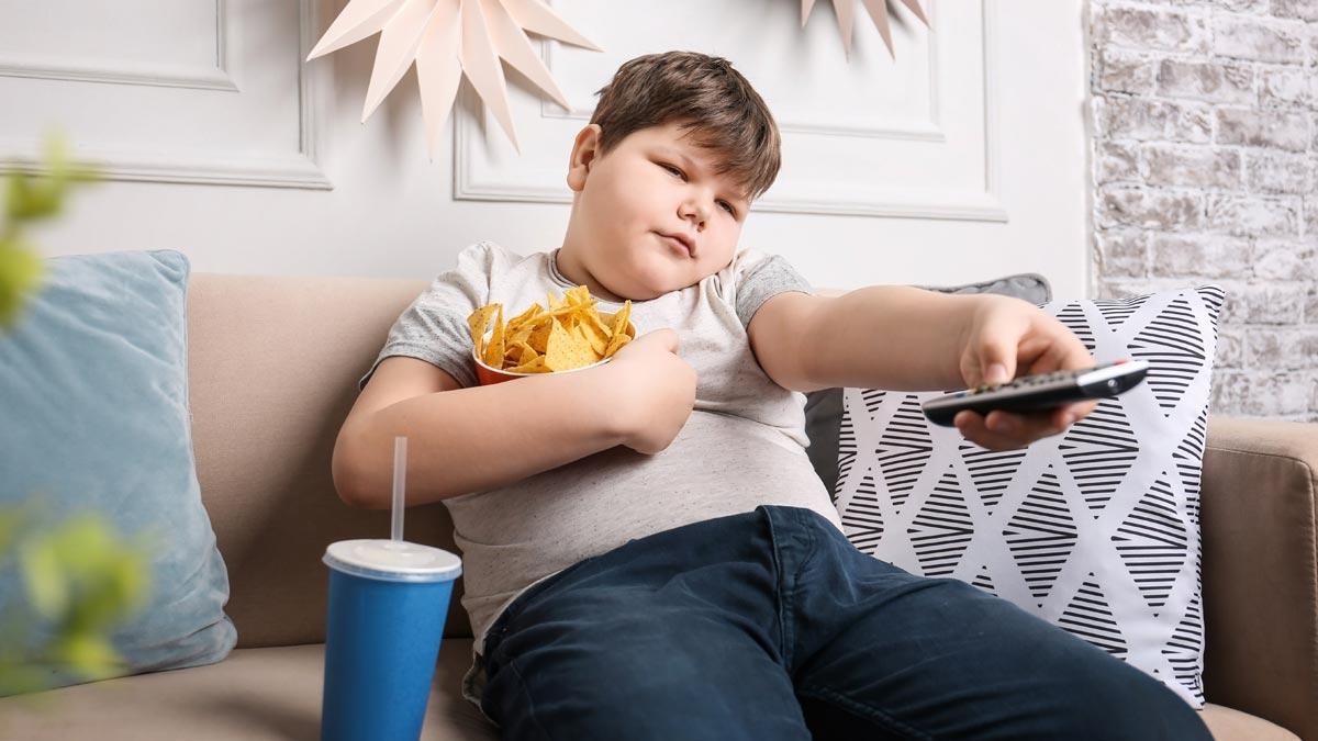 Un niño obeso come mientras ve la televisión.