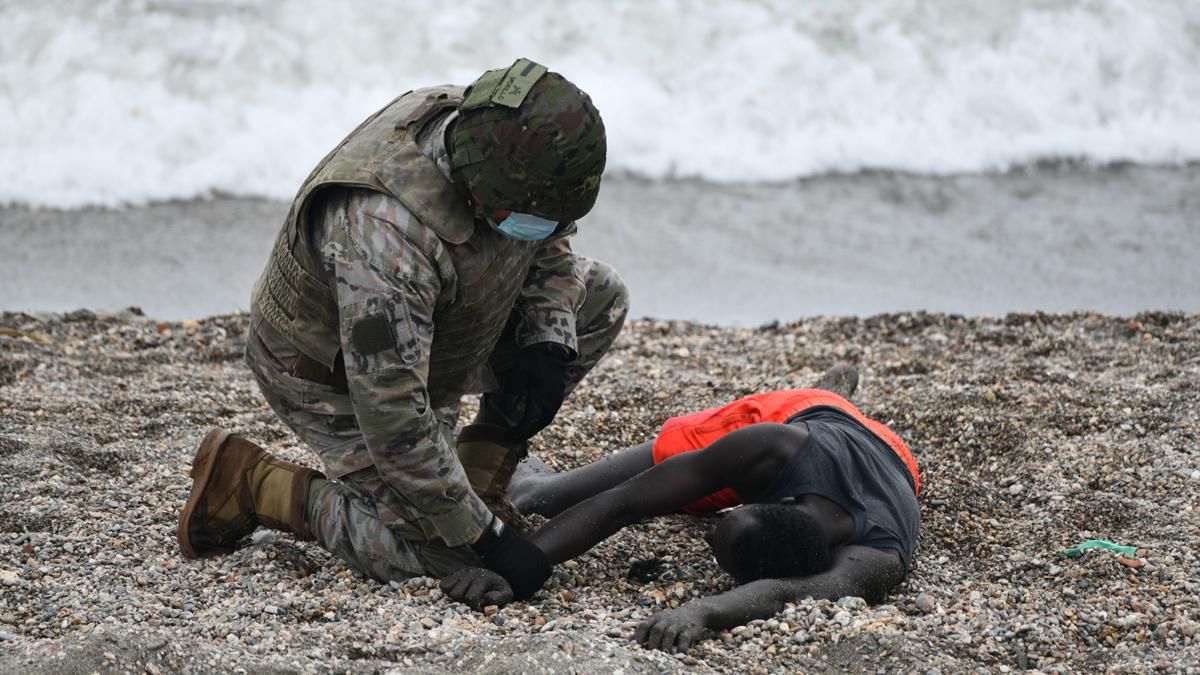 Un militar del ejército español ayuda a una persona tumbada en la orilla en una jornada marcada por las devoluciones en caliente que están efectuando a los migrantes que han entrado en Ceuta.