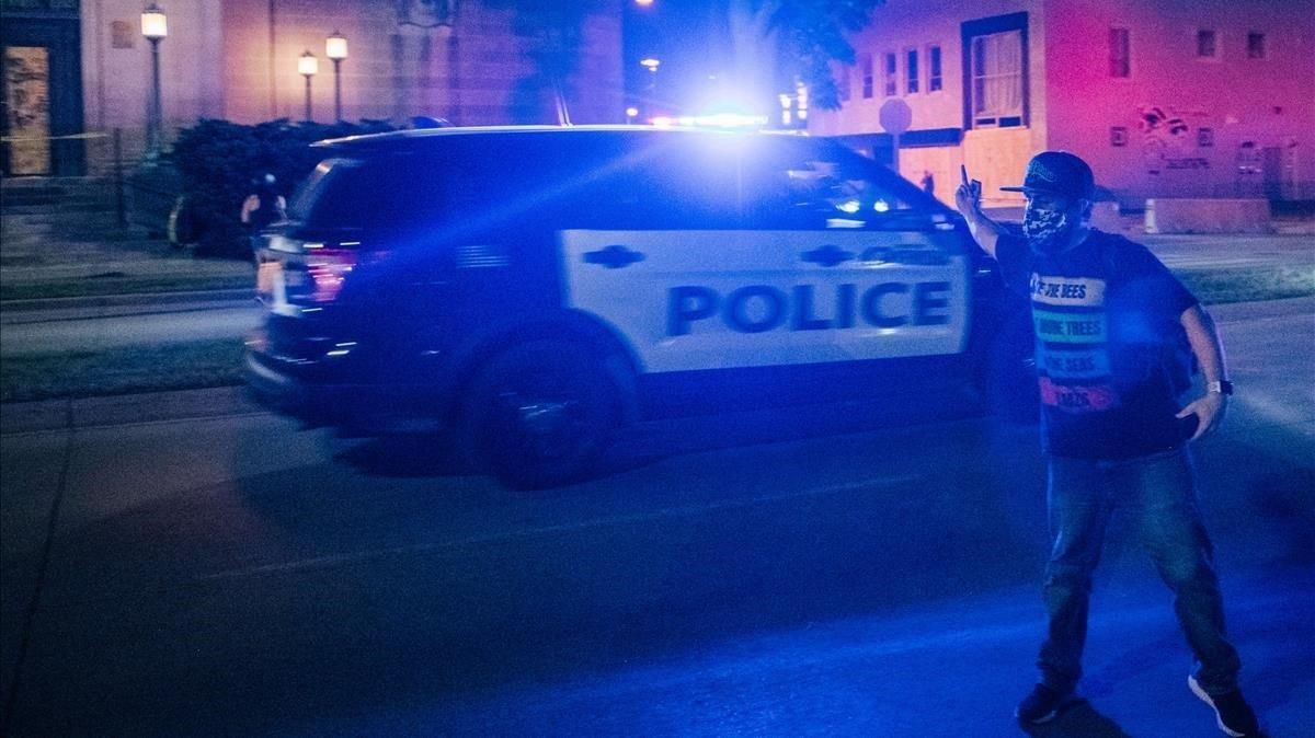 Un manifestante gesticula ante el paso de un vehículo de policía, la noche del miércoles en Kenosha. Un manifestante gesticula ante el paso de un vehículo de policía, la noche del miércoles en Kenosha.
