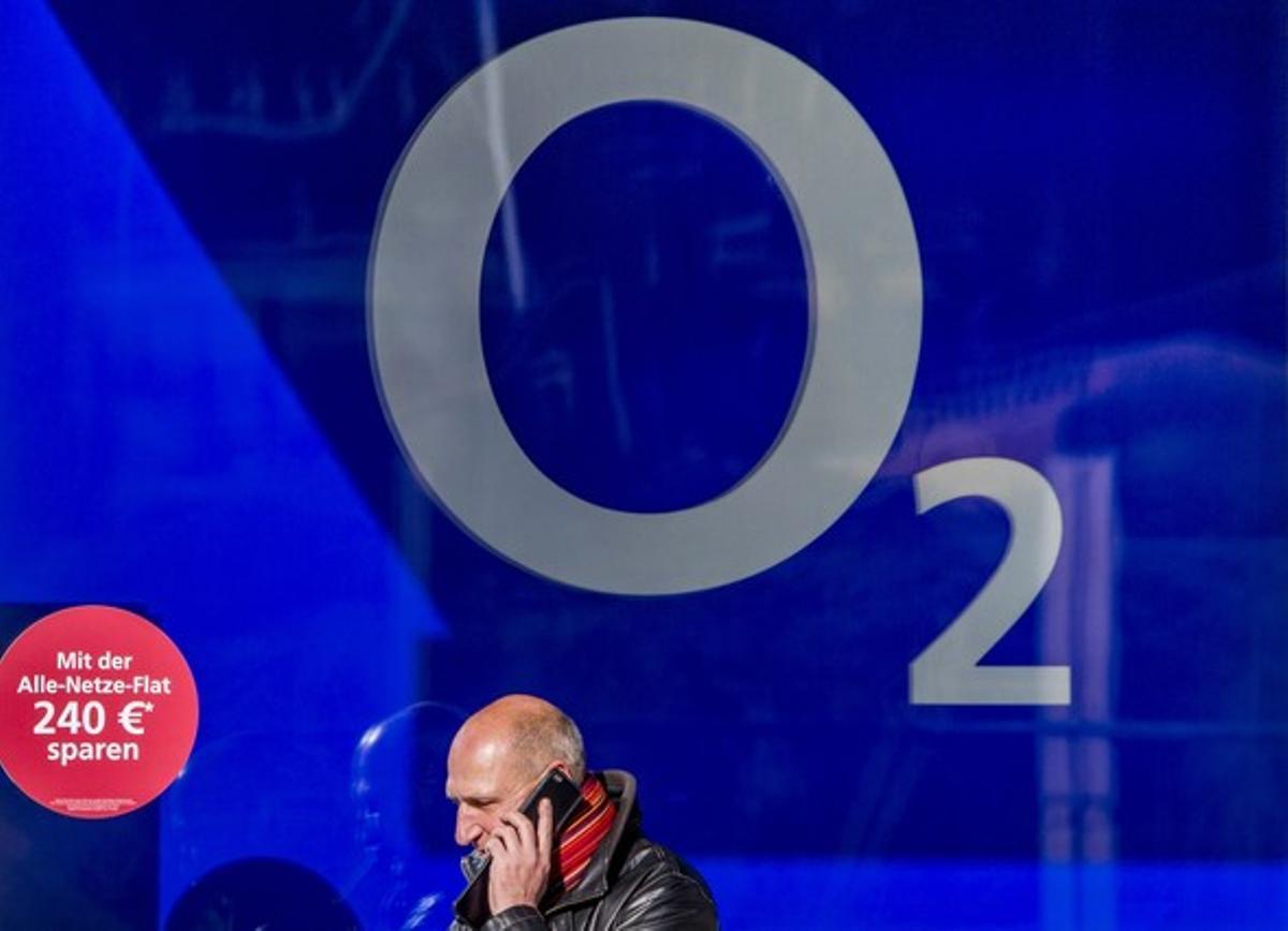 Un hombre pasa hablando por móvil delante de la imagen de O2, filial alemana de Telefónica, en Berlín.