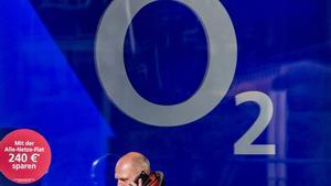 Un hombre pasa hablando por móvil delante de la imagen de O2, filial alemana de Telefónica, en Berlín.