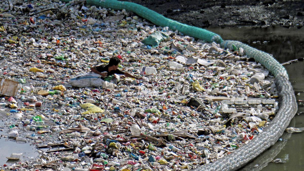 Un hombre recolecta botellas de plástico entre los residuos que una malla impide que alcancen el mar en un río en Cebu (Filipinas).