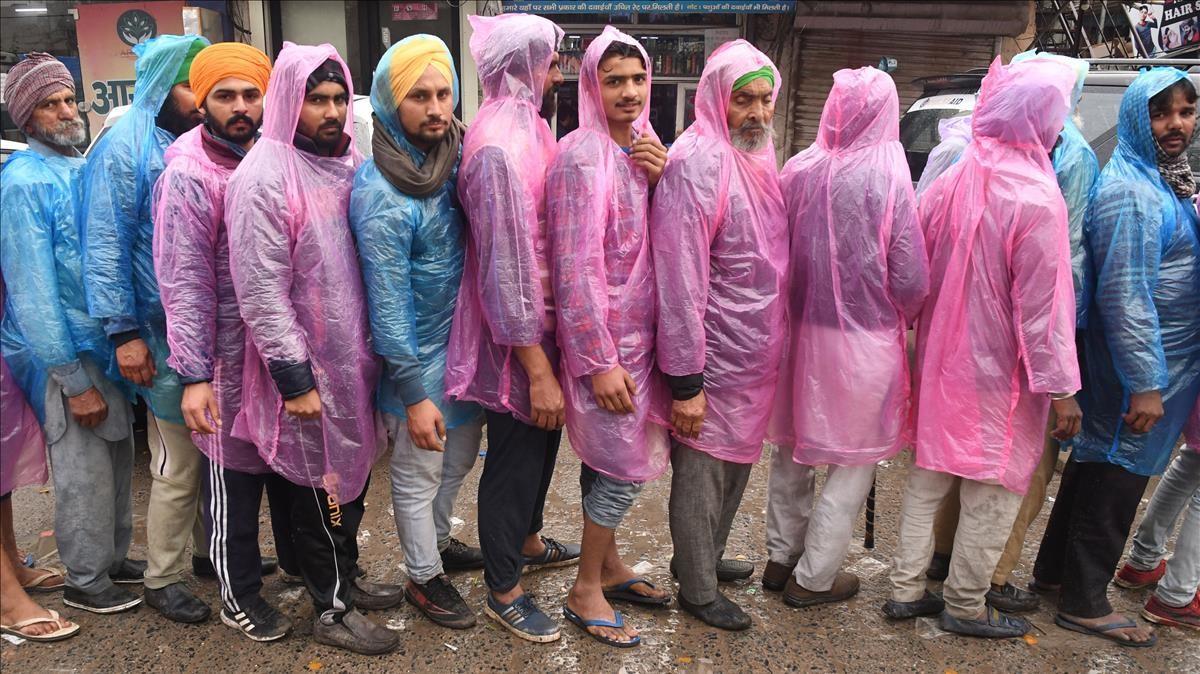 Un grupo de trabajadores hacen cola bajo la lluvia este martes para recibir comida de una cocina comunitaria en Nueva Delhi.