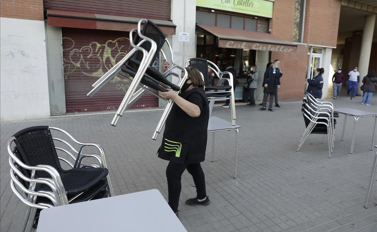 Una trabajadora de un bar del Poblenou recoge las mesas de la terraza tras acabarse el horario en el que puede servir desayunos. Una trabajadora de un bar del Poblenou recoge las mesas de la terraza tras acabarse el horario en el que puede servir desayunos.