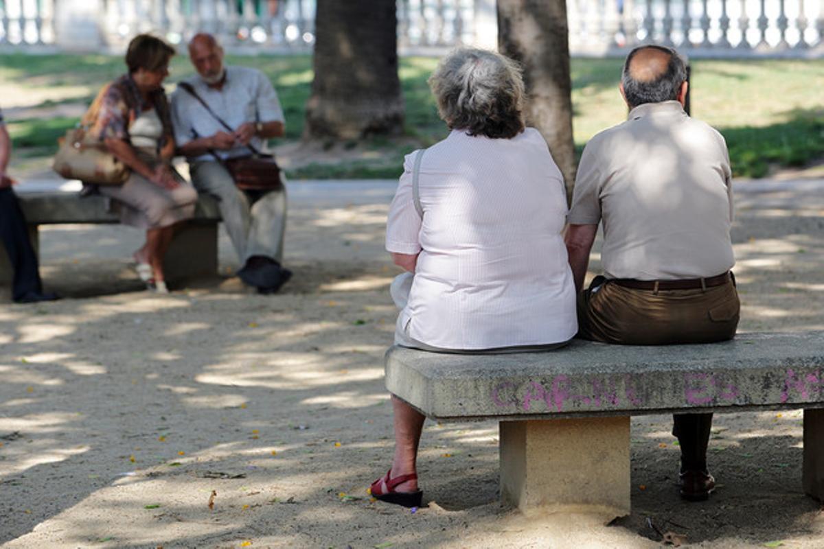 Un grupo de jubilados descansan sentados en unos bancos en una calle de Barcelona.