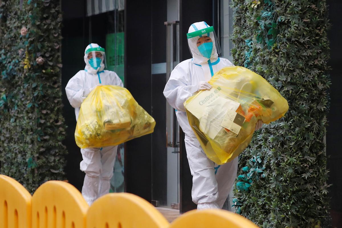 Dos personas con el equipo de protección completo contra el coronavirus en el exterior del hotel donde se han alojado en Wuhan los investigadores de la OMS.