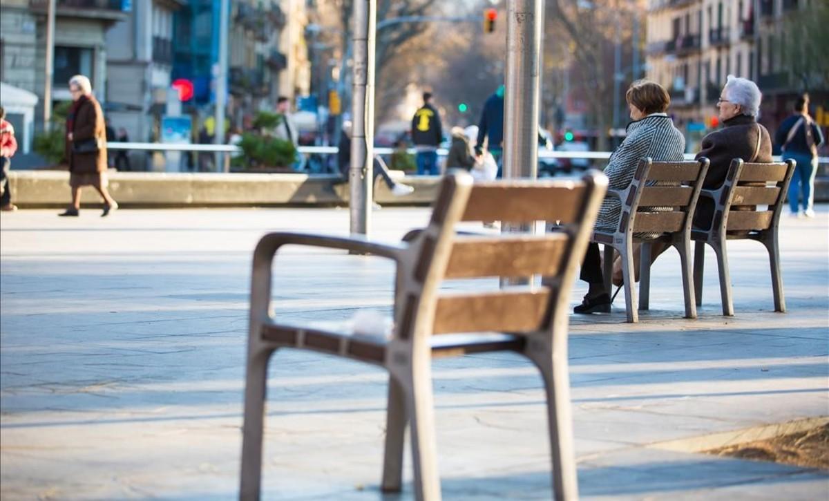 Gente mayor en una calle de Barcelona con mobiliario urbano para sentarse. 