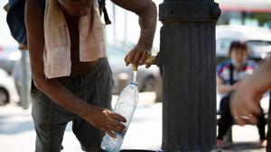 Un hombre llena una botella de agua en una fuente de Barcelona.