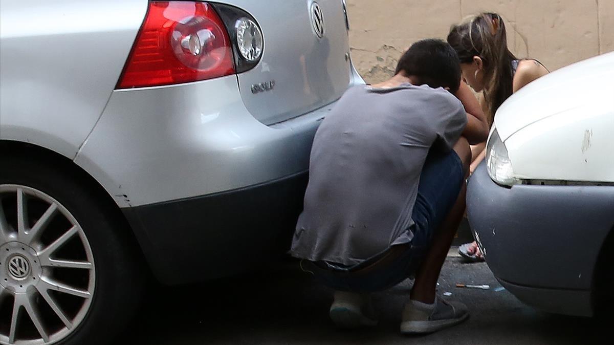 Un hombre y una mujer se preparan inyecciones de heroína entre dos coches, en la calle Egipcíaques, en el Raval, este viernes.