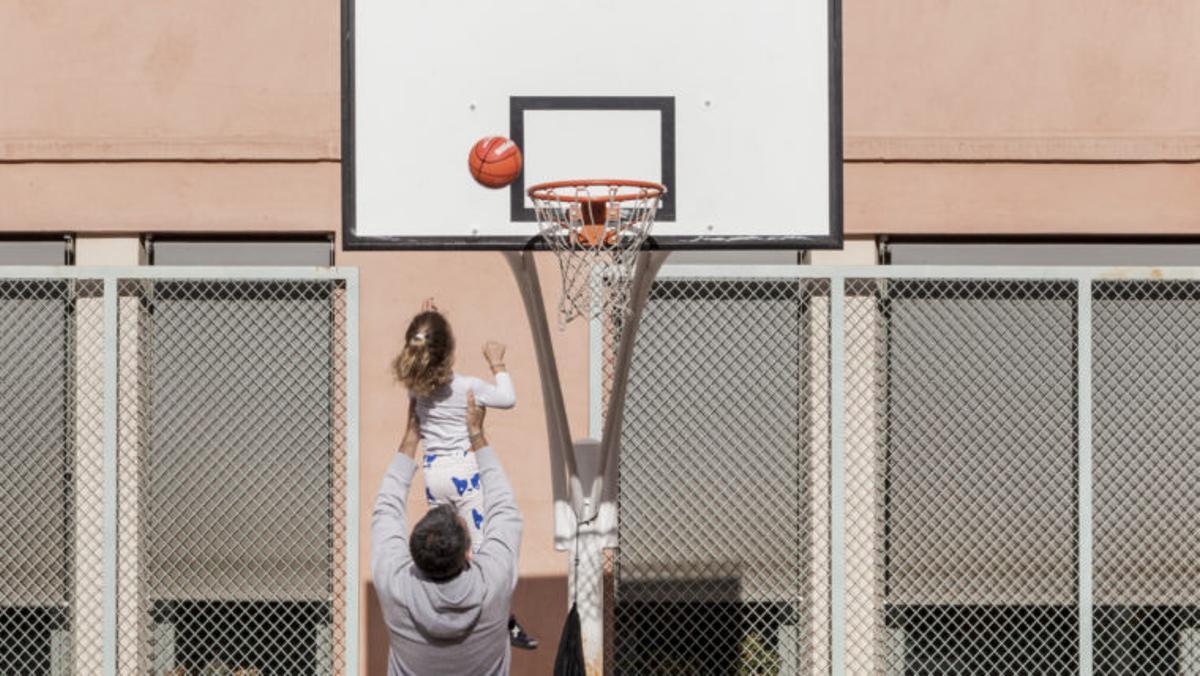 Un padre y su hija juegan a baloncesto en el patio de una escuela.