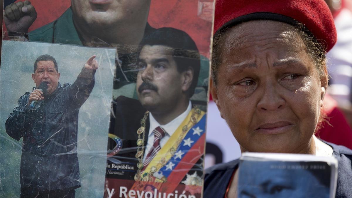 Una partidaria del chavismo llora mientras sostiene imágenes de Chávez y Maduro, durante una marcha por el quinto aniversario de la muerte de Chávez, en Caracas, el 15 de marzo.