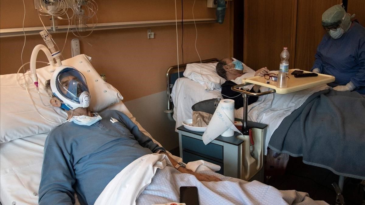 Un paciente con covid lleva una máscara de buceo integral en el Hospital Maria Pia de Turín, el pasado 7 de abril, mientras su compañero de habitación está siendo atendido por un sanitario. Un paciente con covid lleva una máscara de buceo integral en el Hospital Maria Pia de Turín, el pasado 7 de abril, mientras su compañero de habitación está siendo atendido por un sanitario.