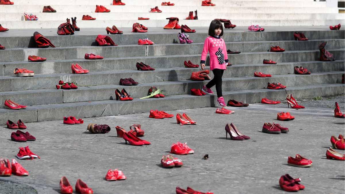 Una niña pasa por una instalación compuesta por zapatos rojos de mujer en una escalera, como símbolo para denunciar la violencia contra las mujeres, en Tirana (Albania).
