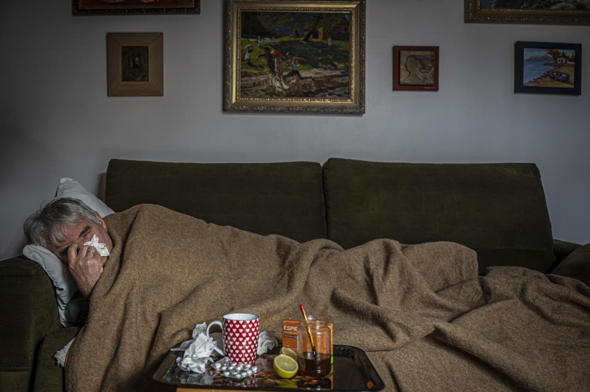 Un hombre con un resfriado en el sofá de su casa.